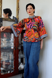 Bold tropical floral blouse featuring vibrant orange, purple, and green hues, paired with a red skirt.
