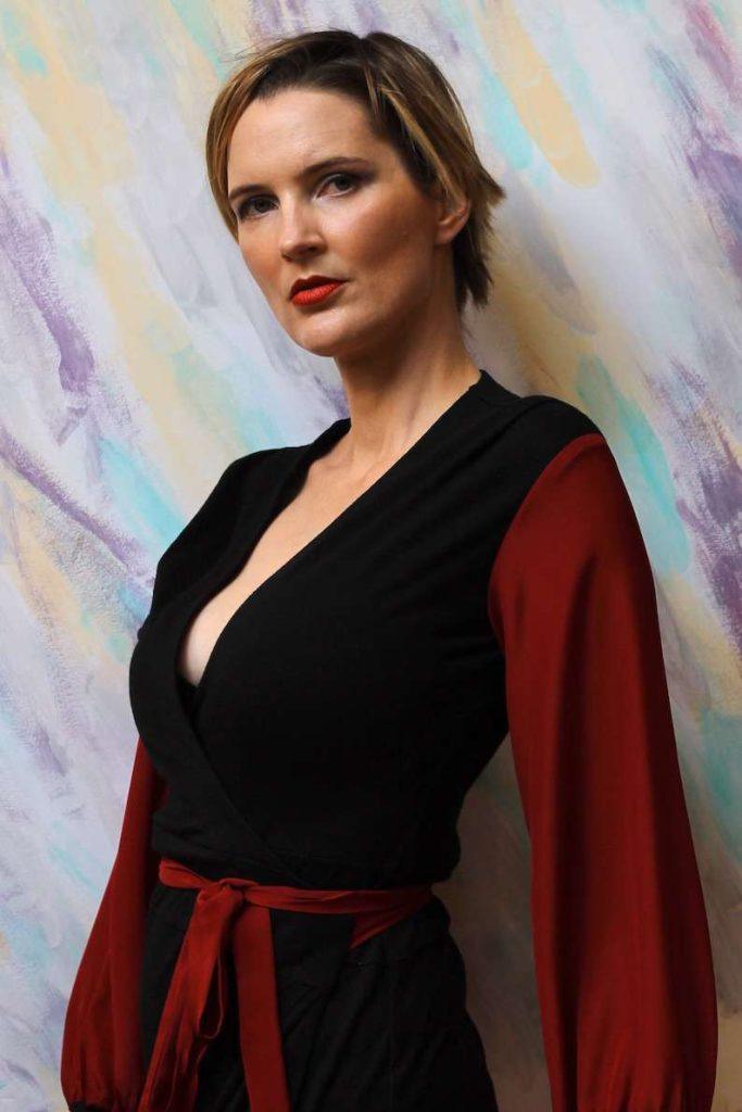 Black wrap dress with long, flowing rust-colored sleeves and a matching rust-colored waist tie, creating a striking contrast in a sleek and elegant silhouette.