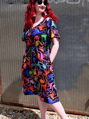 Brightly patterned dress featuring multi-colored abstract animal shapes, worn by a woman against a background that mirrors the vibrant theme, combining playful art with fashion. Designed by Australian designer brand Streborclothing.