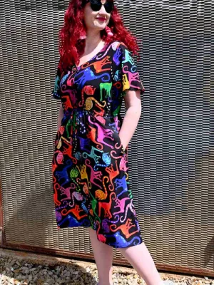 Brightly patterned dress featuring multi-colored abstract animal shapes, worn by a woman against a background that mirrors the vibrant theme, combining playful art with fashion. Designed by Australian designer brand Streborclothing.