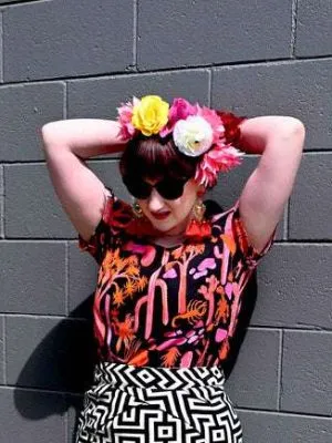 Woman wearing a vibrant black top with a pink and orange desert-themed print, posed against a similarly themed background, emphasizing the bold, artistic nature of Strebor's style. Designed by Australian designer brand Streborclothing.