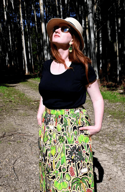 This skirt showcases a complex pattern with elements of flora, including leaves, flowers, and abstract natural shapes in shades of green, red, and yellow. The design appears dense and rich, resembling an intricate forest scene. Designed by Australian designer brand Streborclothing.