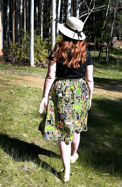 This skirt showcases a complex pattern with elements of flora, including leaves, flowers, and abstract natural shapes in shades of green, red, and yellow. The design appears dense and rich, resembling an intricate forest scene. Designed by Australian designer brand Streborclothing.