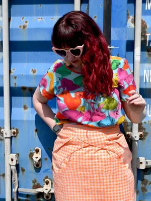 A colorful top displaying an abstract pattern of vibrant swans in reds, greens, and pinks, against a light blue background, with each swan in a unique position, adding movement and whimsy. Designed by Australian designer brand Streborclothing.