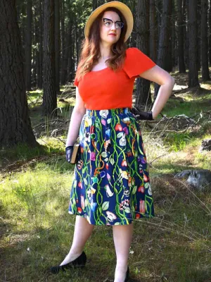 Woman in a forest scene wearing a dark blue skirt with a lively floral and vine print, blending earthy elements with an artistic twist in nature-inspired surroundings. Designed by Australian designer brand Streborclothing.