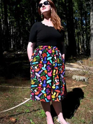 The skirt features a vibrant mushroom pattern with various brightly colored mushrooms in red, yellow, blue, pink, and green on a black background. This playful design adds a whimsical and organic feel to the outfit. Designed by Australian designer brand Streborclothing.